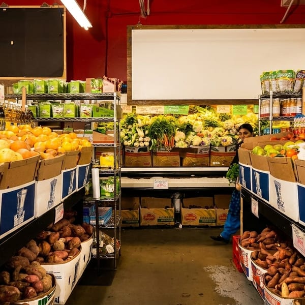 A grocery store aisle filled with fresh produce, including sweet potatoes, oranges, and apples.