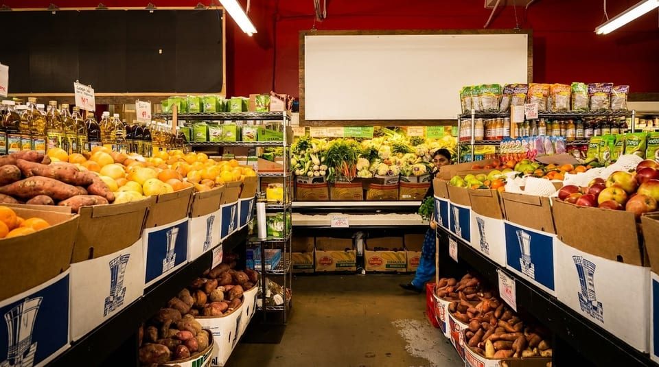 A grocery store aisle filled with fresh produce, including sweet potatoes, oranges, and apples.