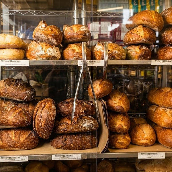 Artisan bread loaves displayed on shelves in a bakery or grocery store, with beverages in the background.