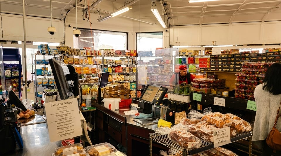 A bakery interior with a counter displaying baked goods, a cashier, and shelves stocked with various products.